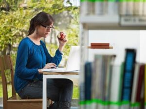 Female College Student Studying In A Library, Eating A Red Apple Fully Energized This Spring Semester