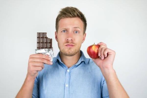 Man holding a chocolate bar and apple, making a choice