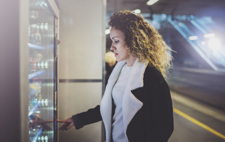 Attractive woman on transit platform using a modern beverage vending machine.Her hand is placed on the dial pad and she is looking on the small display screen